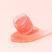 Heimish Ever Glow All Night Lip Mask coral jar on a swirl of peach balm on a soft pink background