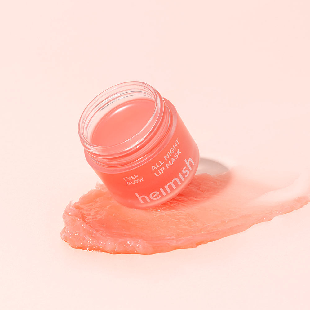 Heimish Ever Glow All Night Lip Mask coral jar on a swirl of peach balm on a soft pink background