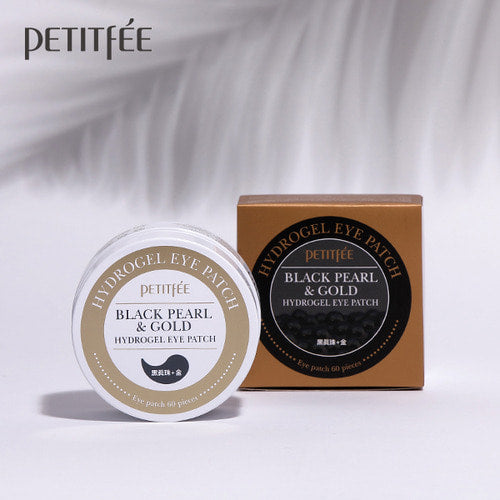 Petitfee Black Pearl & Gold Hydrogel Eye Patch jar lid and bronze box under soft leaf shadows