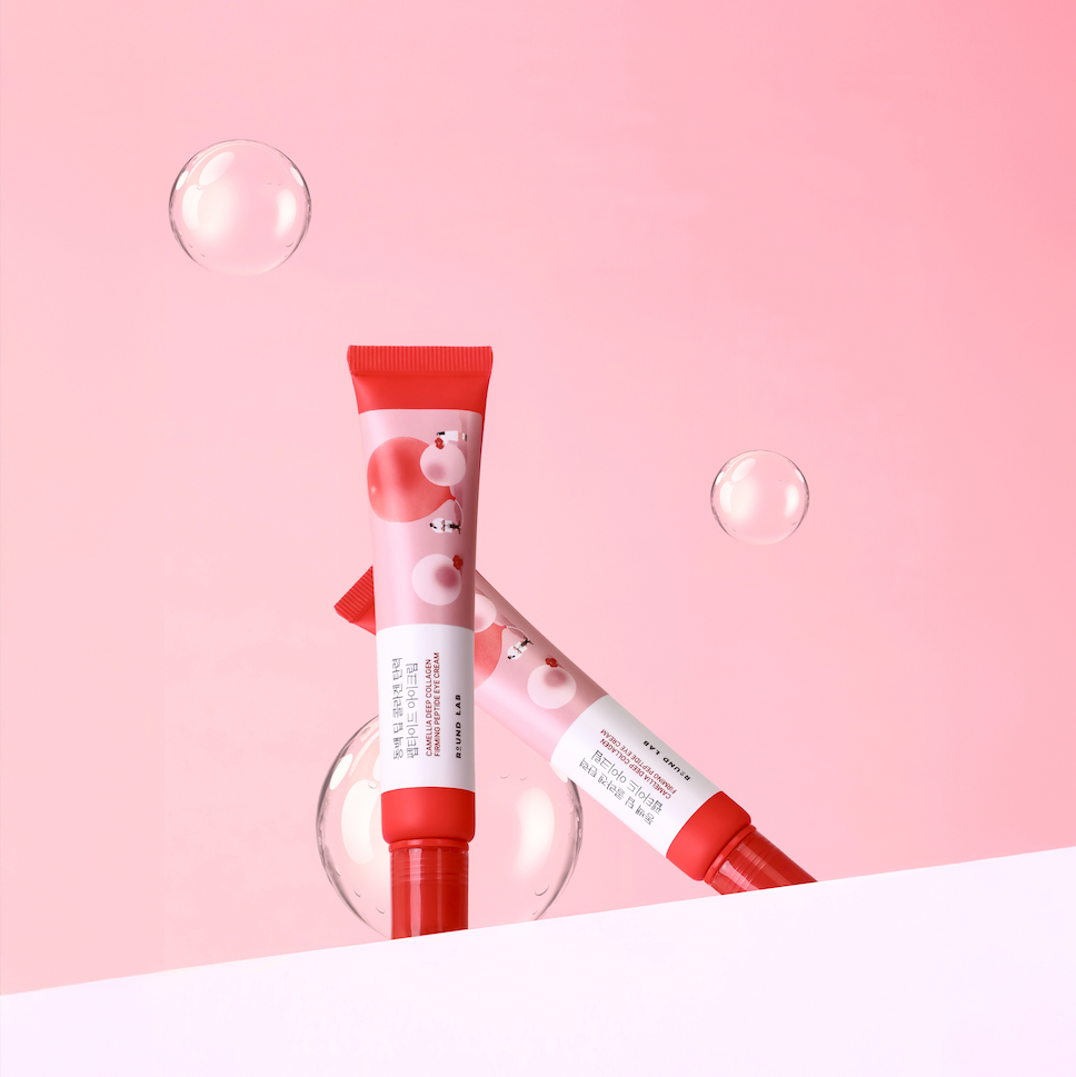 Round Lab Camellia Deep Collagen Eye Cream, two pink and red tubes posed with bubbles on a pink backdrop