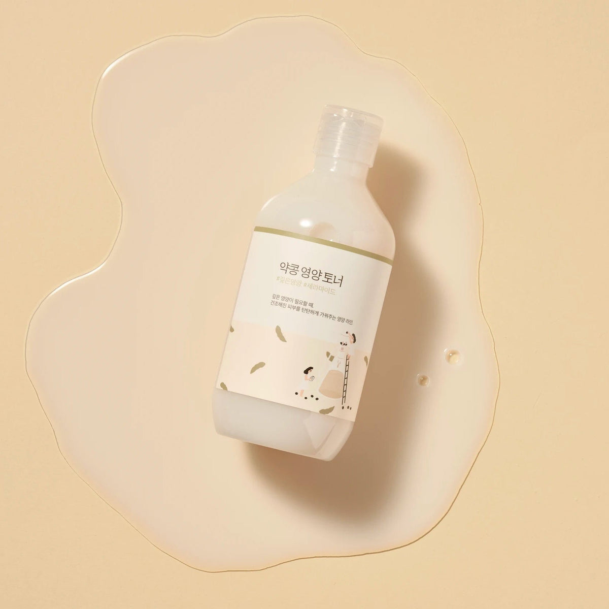 Round Lab Soybean Nourishing Toner bottle lying in a pool of the clear toner on a beige background