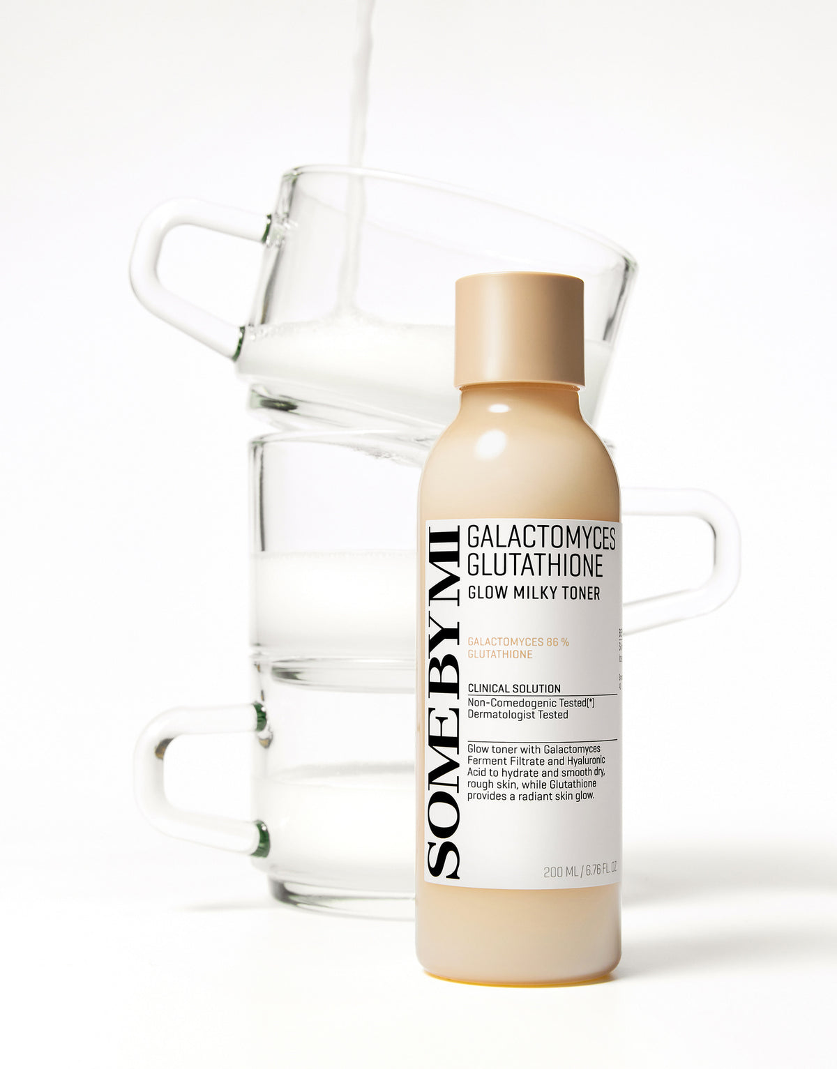 Some By Mi Galactomyces Glutathione Glow Milky Toner bottle in front of stacked glass cups of milk