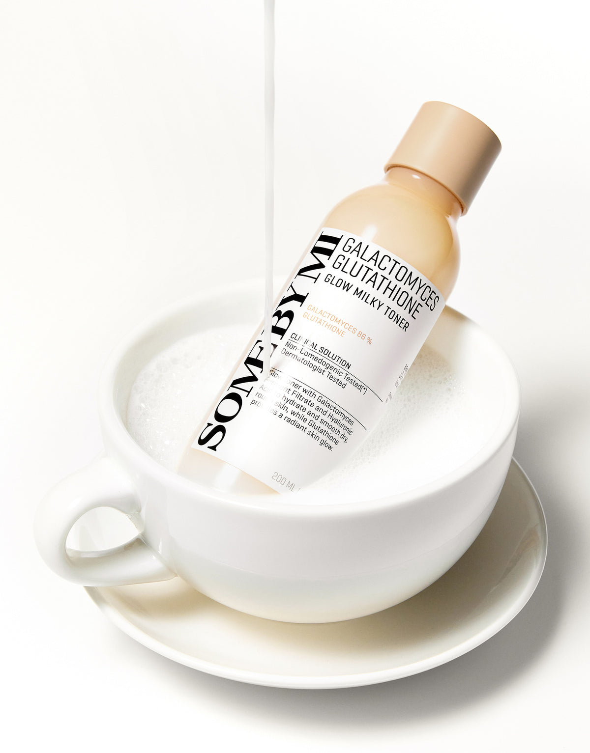 Some By Mi Galactomyces Glutathione Glow Milky Toner bottle in a white cup with milky foam being poured