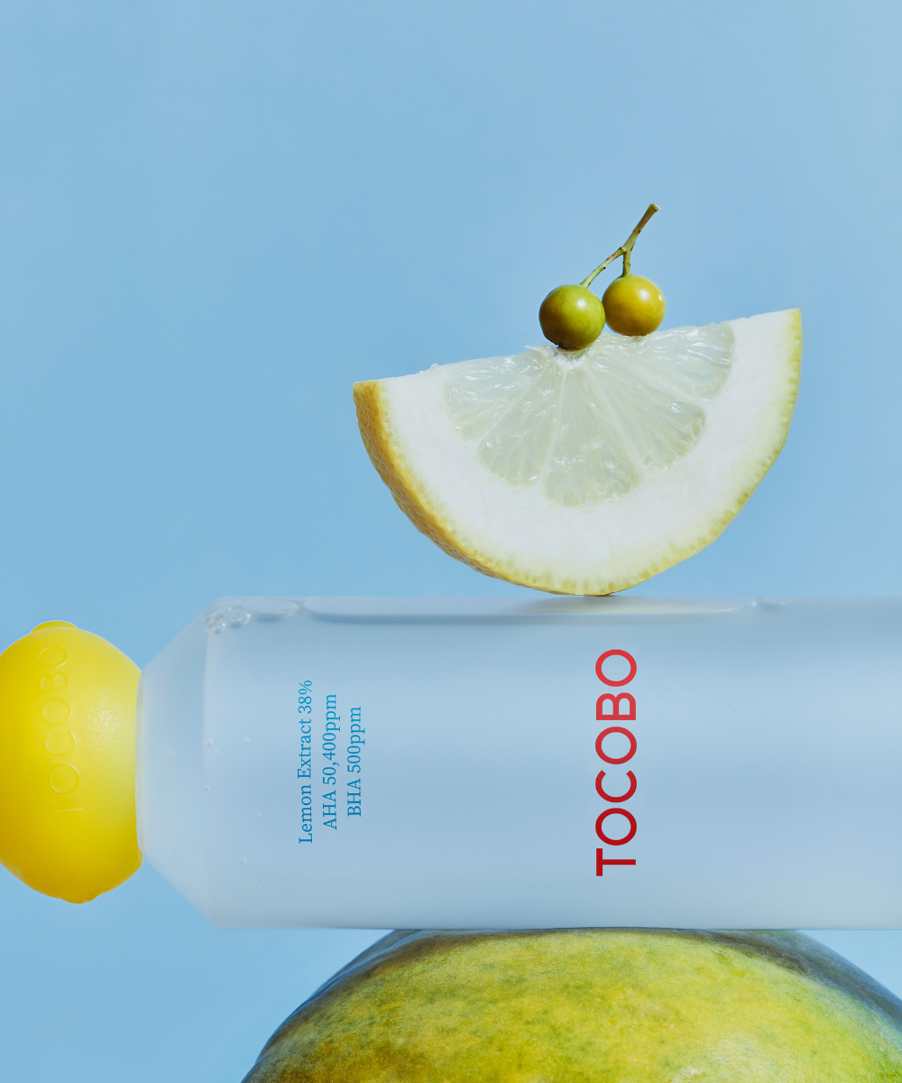 Tocobo AHA BHA Lemon Toner bottle lying on a lemon with a lemon slice on top, sky-blue background